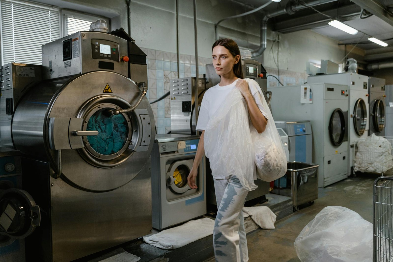 A Woman Carrying a Plastic Full of Clothes Inside the Laundry Facility